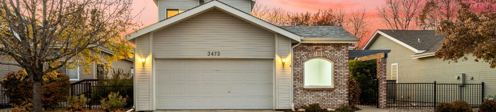 Front view of a suburban house in Altadena with a closed white garage door, brick and siding exterior, and warm outdoor lighting during sunset, highlighting professional garage door services.