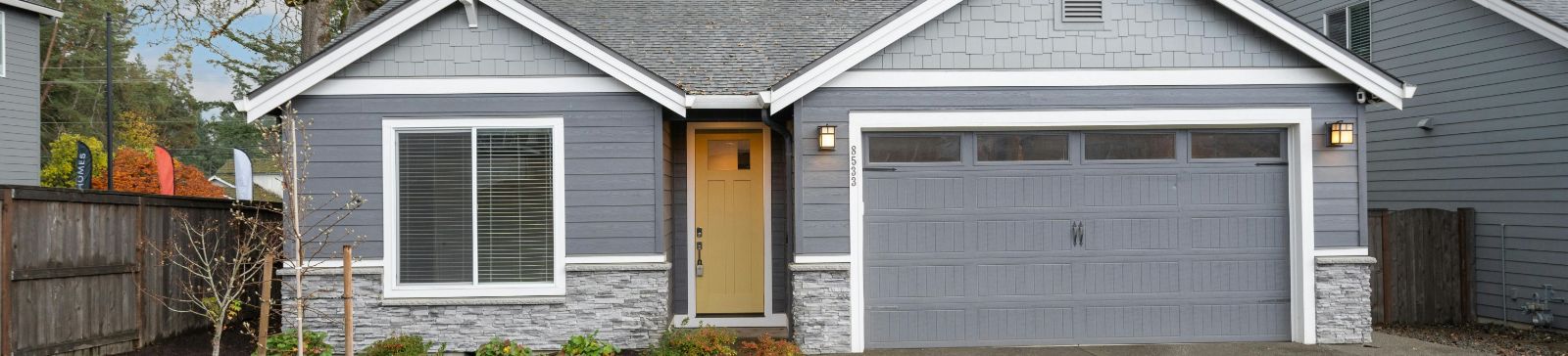Front exterior of a modern single-story house in Altadena featuring a gray paneled garage door, stone and wood accents, and a yellow entry door, showcasing residential garage door solutions.